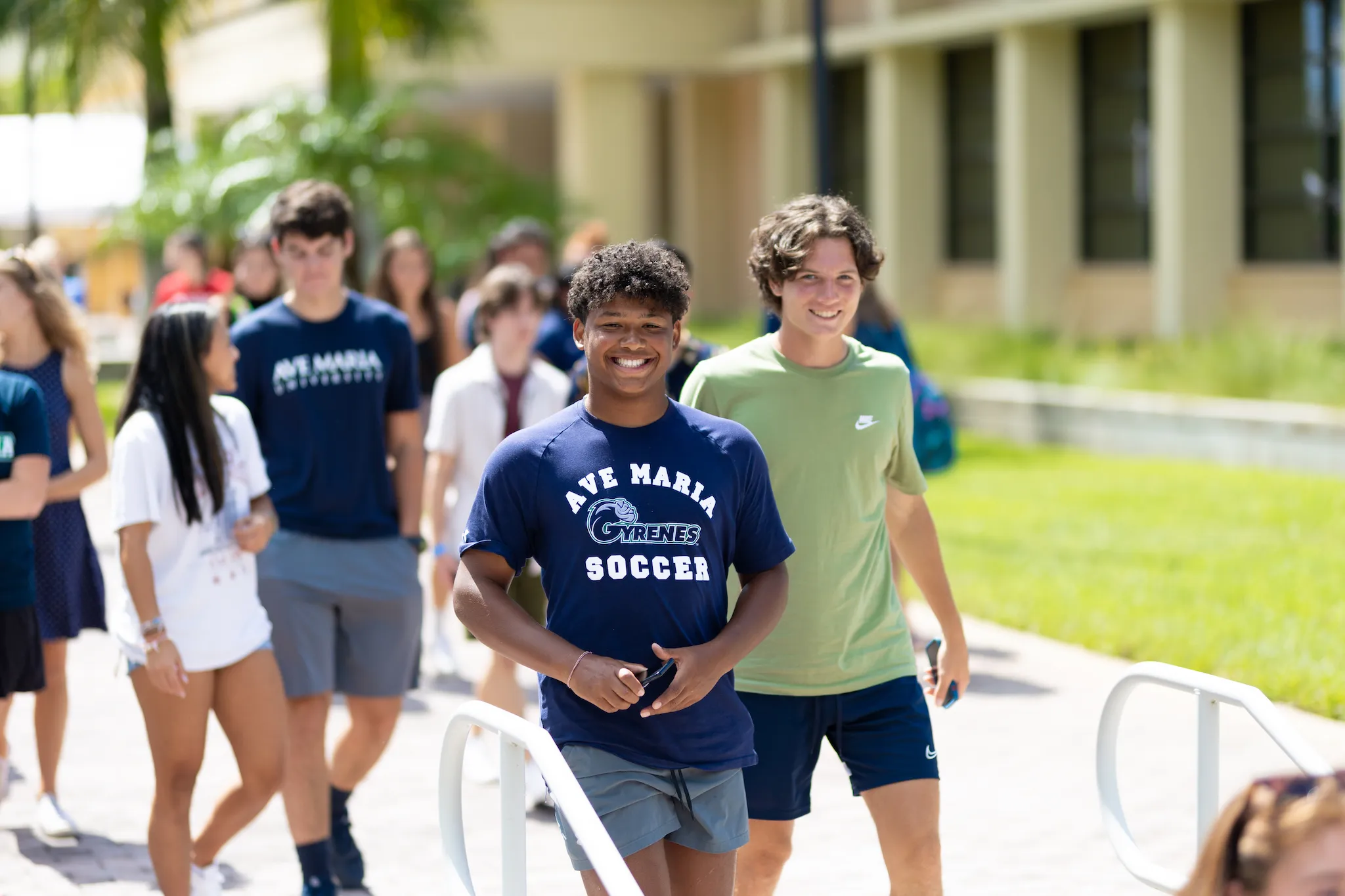 Ave Maria students walking together outside a campus building, one wearing a Gyrenes soccer shirt
