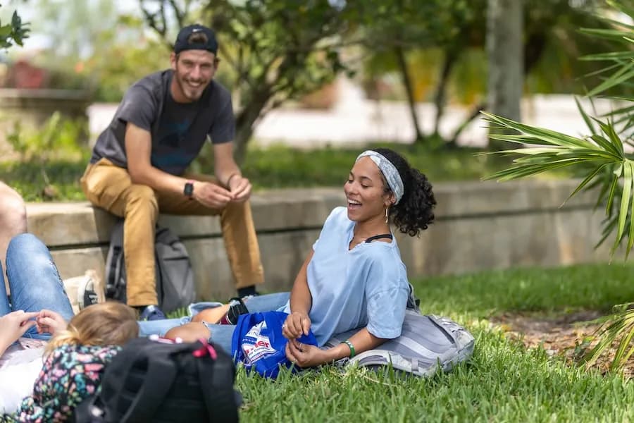 Ave Maria students sitting on the grass together, laughing, on a sunny day on campus